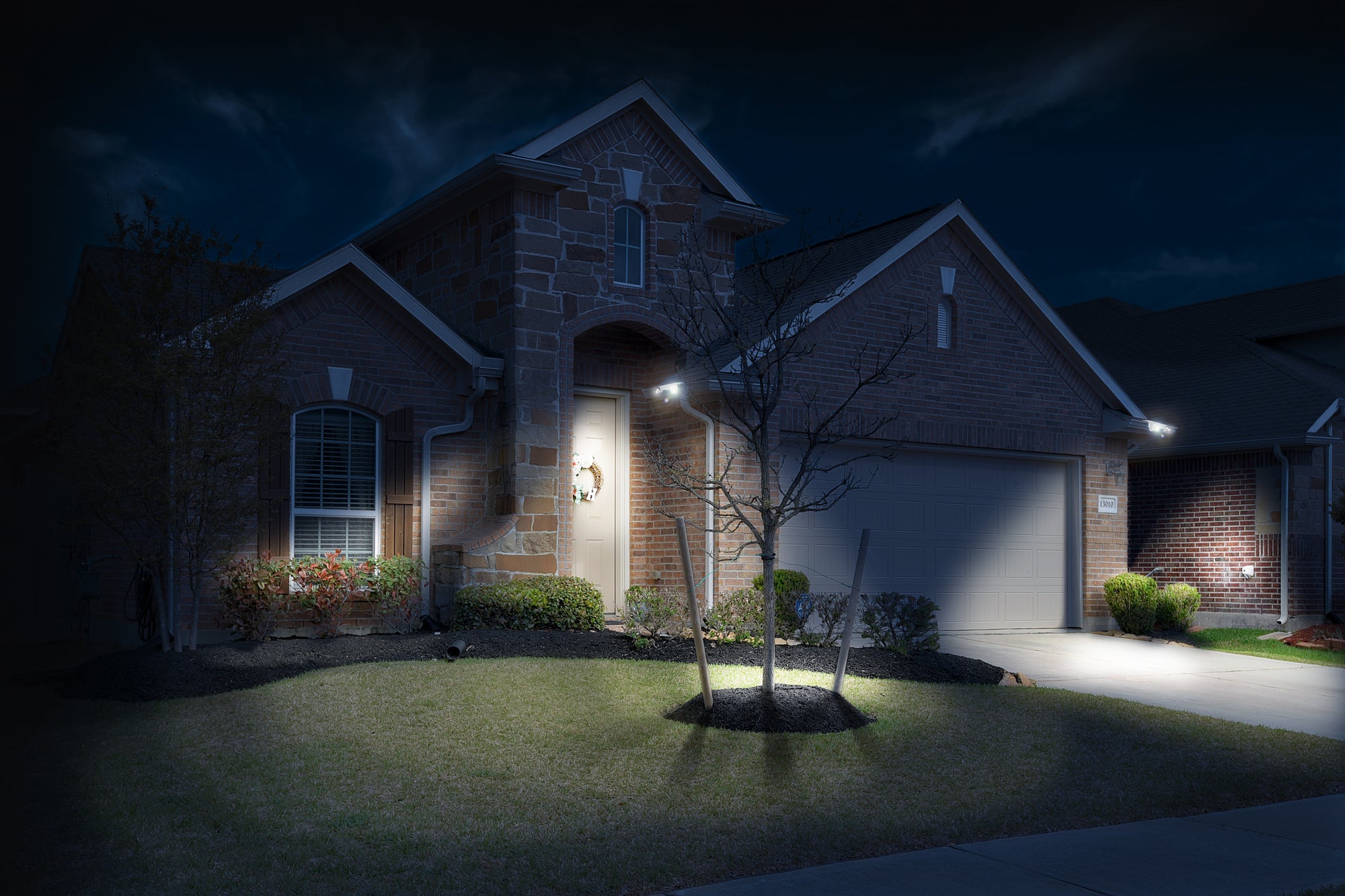 Brick and stone built house shown at night with two EZ Home Security Solar Gutter lights illuminating the front of the house and driveway