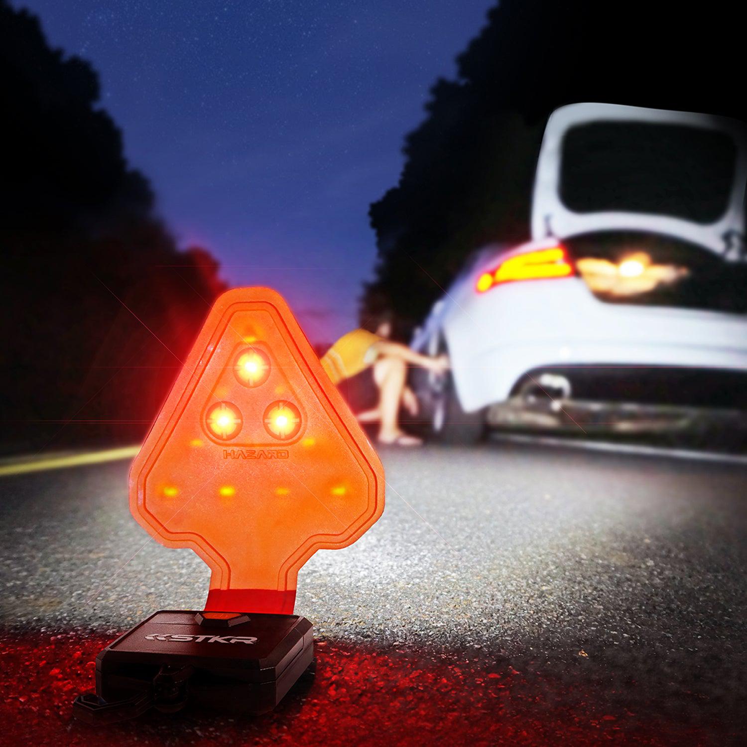 STKR FLEXIT Auto lighting up a female inspecting her car's driver's side rear tire in a nighttime roadside setting. 3 red LEDs are facing oncoming traffic to warn them of the emergency.