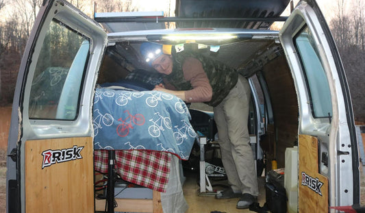 Male standing inside of a conversion van with headlamp on and an under hood light right above him. both products by STKR Concepts.