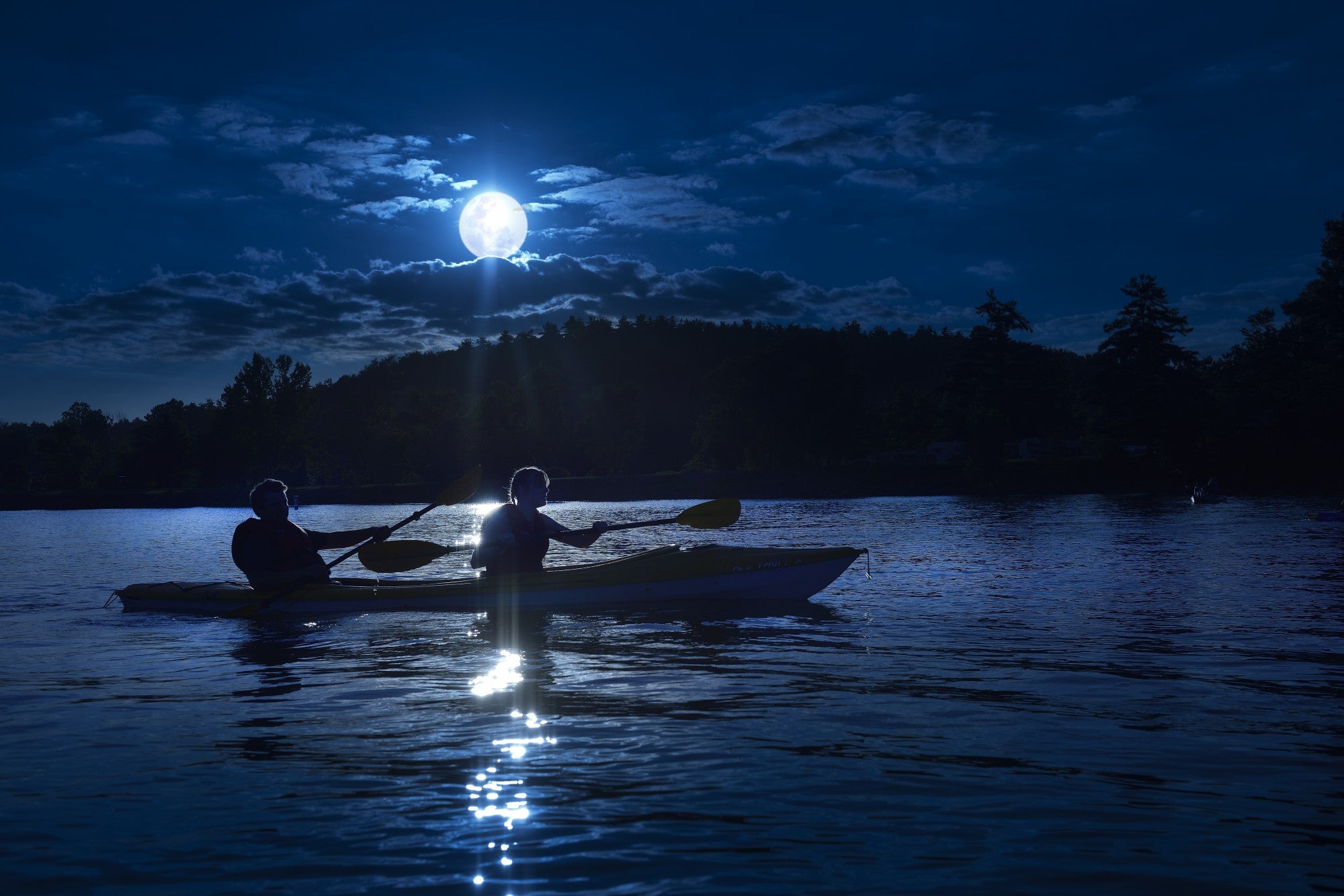 two people canoeing at night on a lake. Dark scene just lit by the moon.