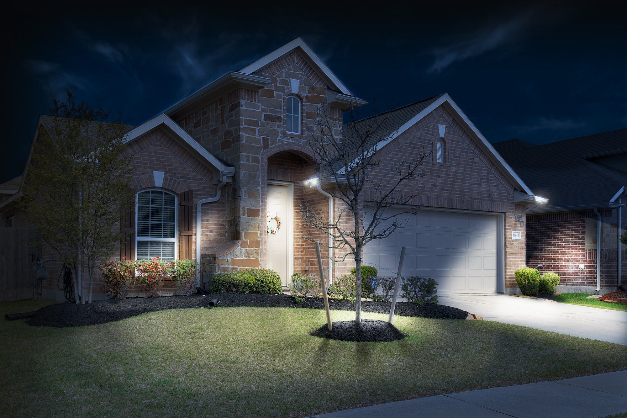 Brick home at night with front yard lit up by gutter lights by STKR