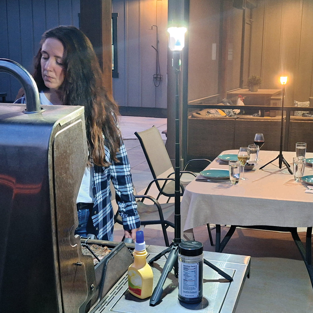 Woman grilling outdoors with a FLi-MORPHE lighting up here grilling experience. In the background, an outdoor table with place settings and wine glasses full. A FLi-MORPHE set to warm light sitting in the middle of the table.