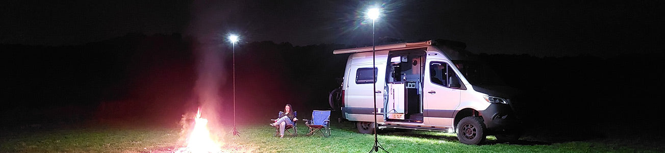 night time van camping scene. female sitting by the fire. Campsite lit up by two FLi OVER-LANDERs
