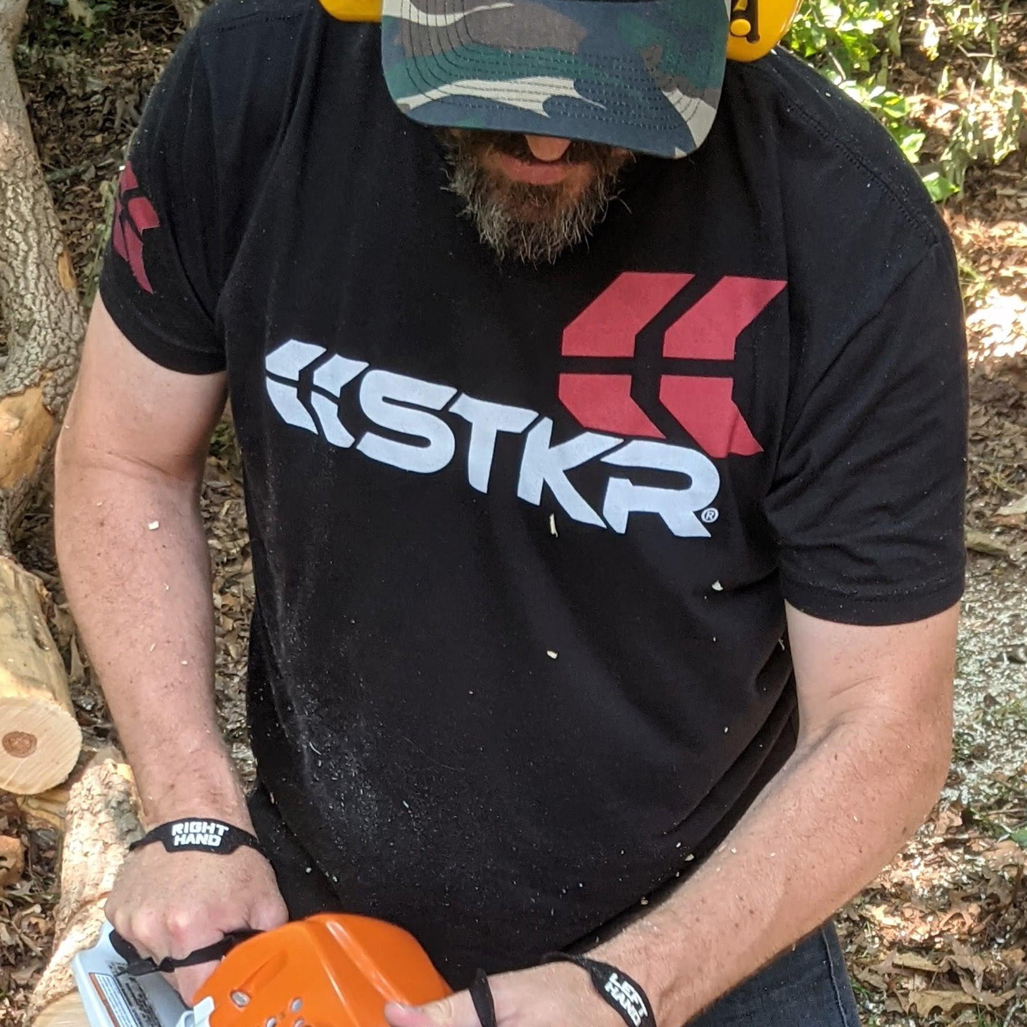 bearded man cutting with a chainsaw wearing an STKR T-shirt